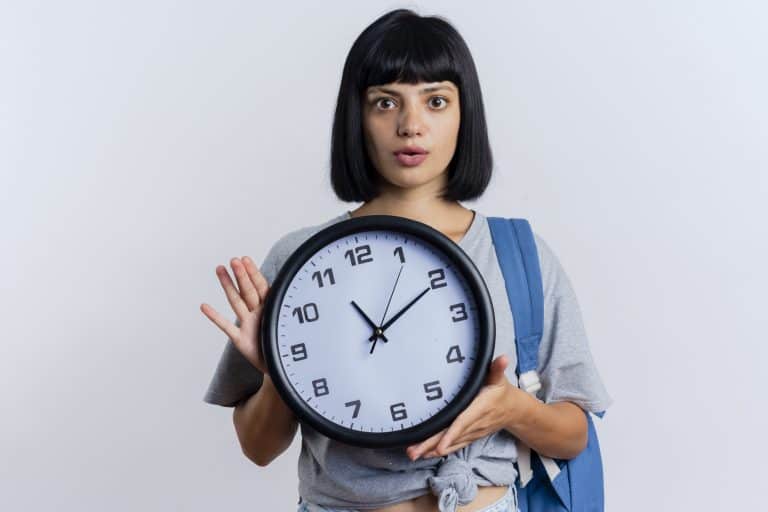 Shocked young woman holding clock